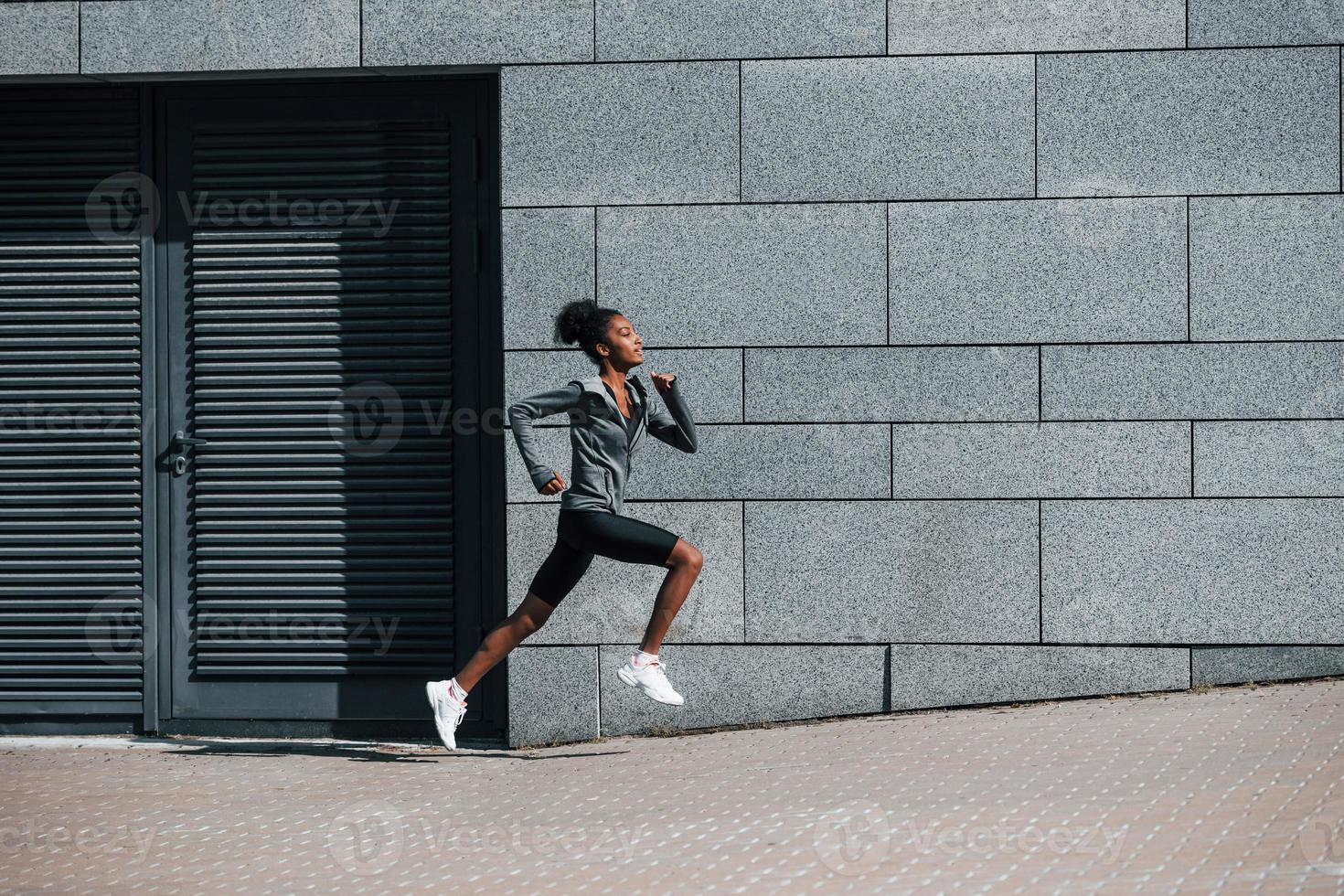 Side view of young african american woman in sportive clothes that runs near wall photo