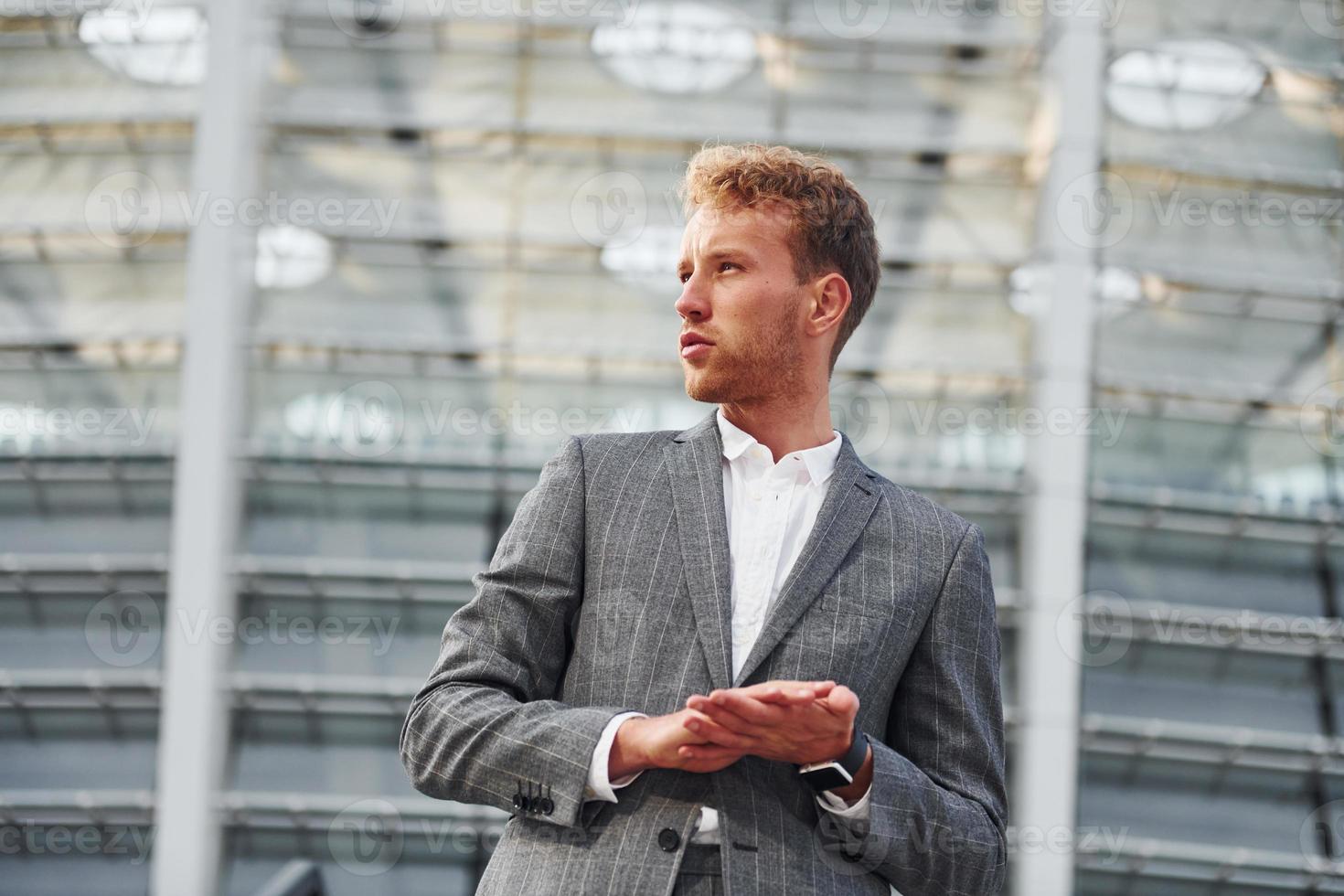 On the stairs of stadium. Young businessman in grey formal wear is outdoors in the city photo