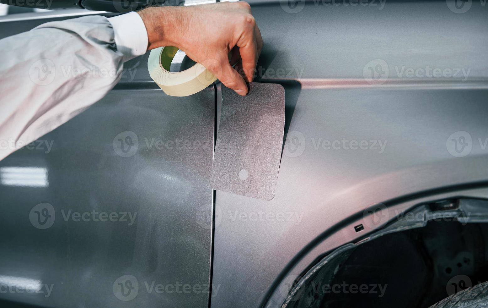 Applying new color. Caucasian automobile repairman in uniform works in garage photo