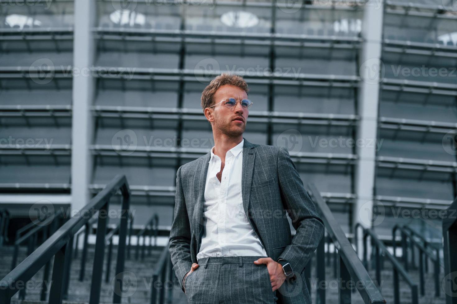 On the stairs of stadium. Young businessman in grey formal wear is outdoors in the city photo