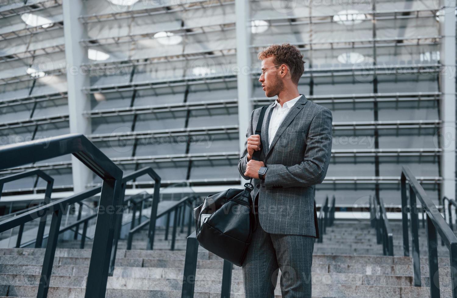 On the stairs of stadium. Young businessman in grey formal wear is outdoors in the city photo