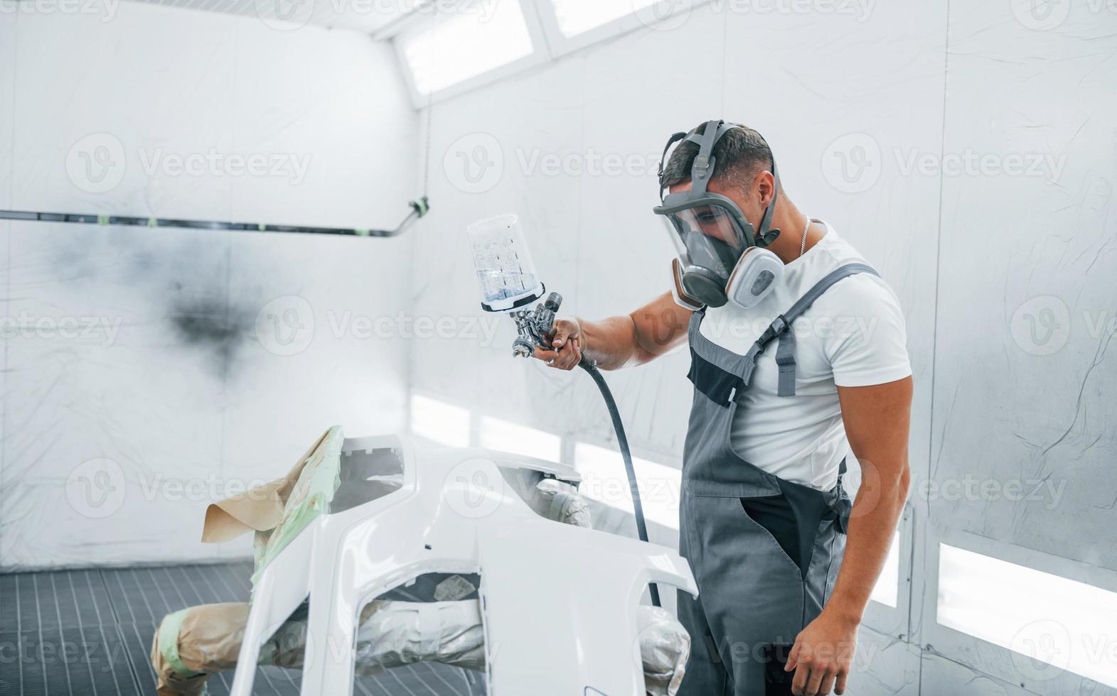 Uses painting gun. Caucasian automobile repairman in uniform works in garage photo