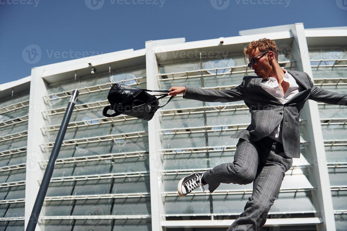 Jumping and celebrating success. Young businessman in grey formal wear is outdoors in the city photo