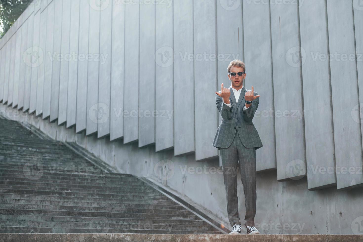 Posing for a camera. Young businessman in grey formal wear is outdoors in the city photo