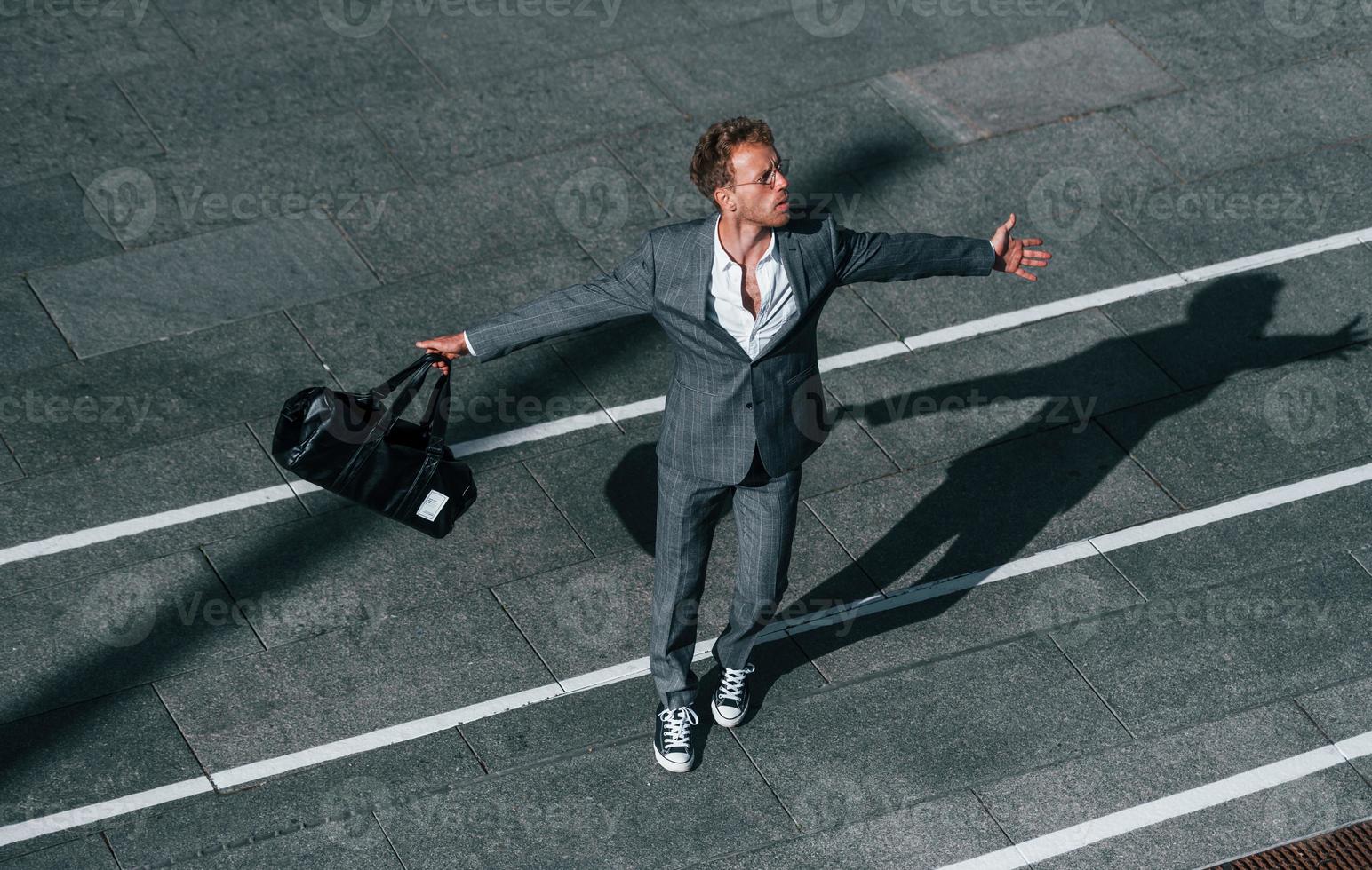 bailando, celebrando el éxito. un joven hombre de negocios con ropa formal gris está al aire libre en la ciudad foto