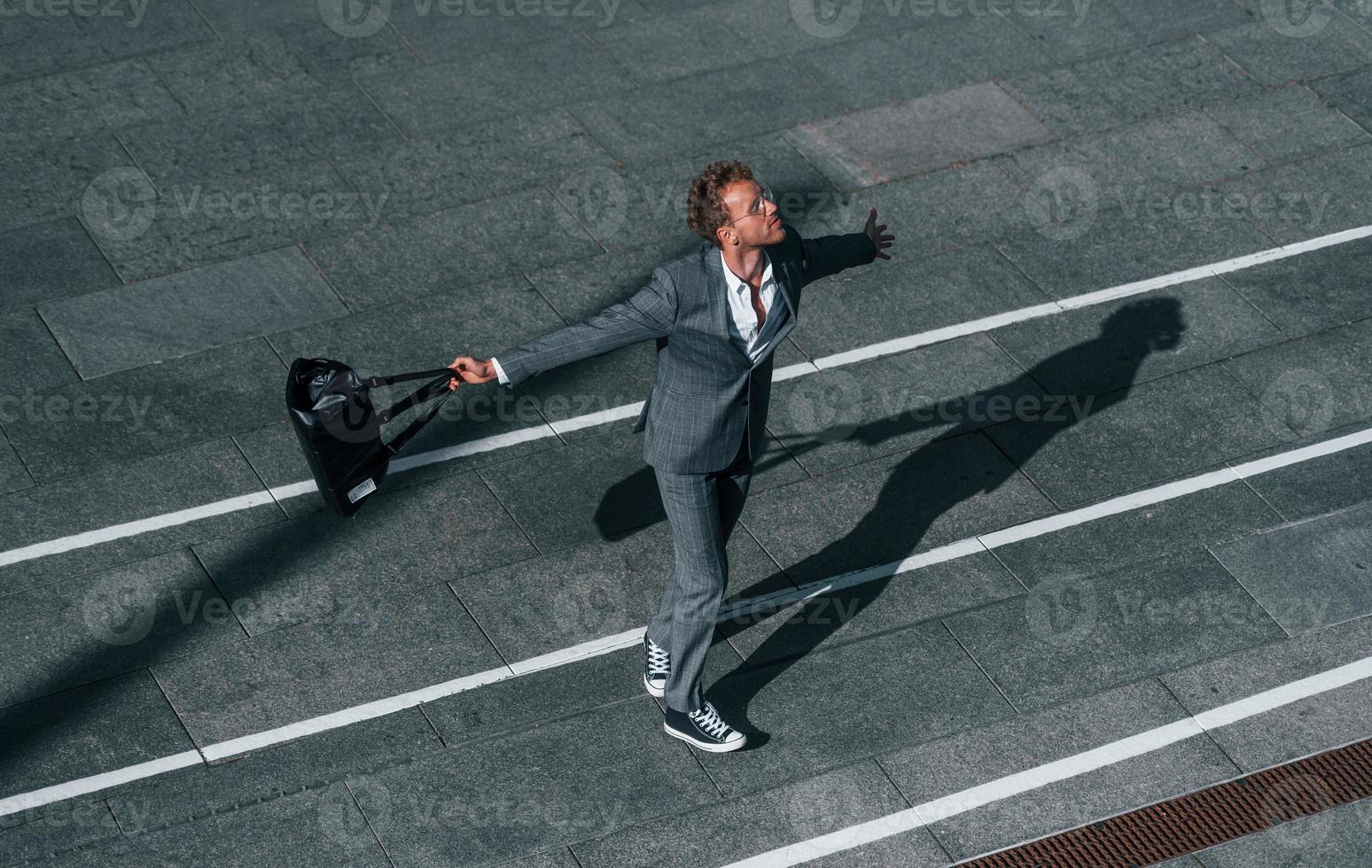 bailando, celebrando el éxito. un joven hombre de negocios con ropa formal gris está al aire libre en la ciudad foto