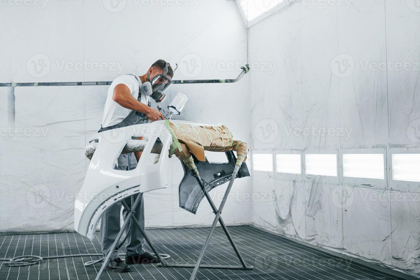 Uses painting gun. Caucasian automobile repairman in uniform works in garage photo