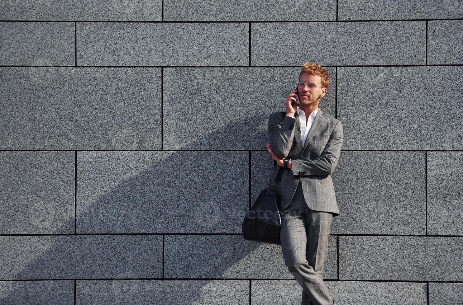 contra la pared gris. un joven hombre de negocios con ropa formal gris está al aire libre en la ciudad foto