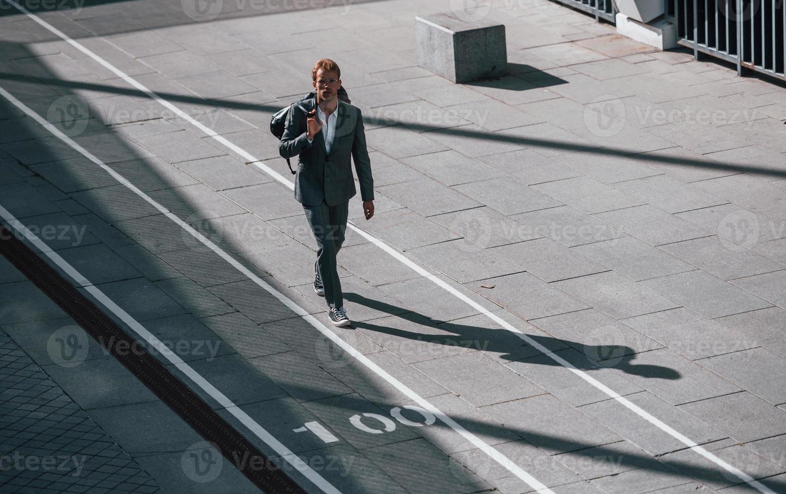 Walks on the road. Young businessman in grey formal wear is outdoors in the city photo