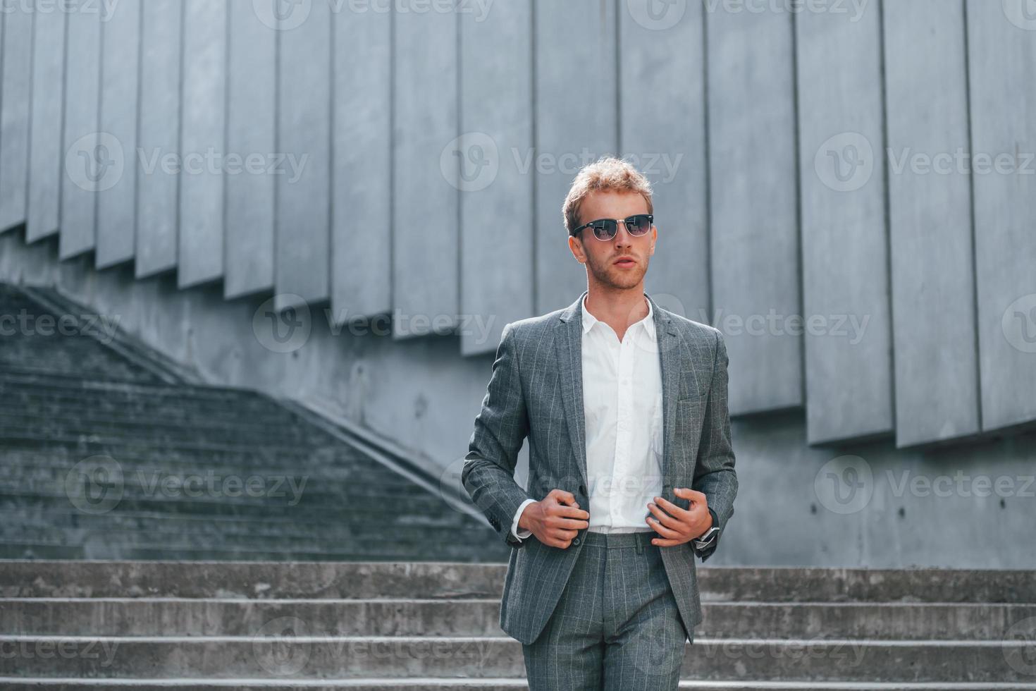 Posing for a camera. Young businessman in grey formal wear is outdoors in the city photo