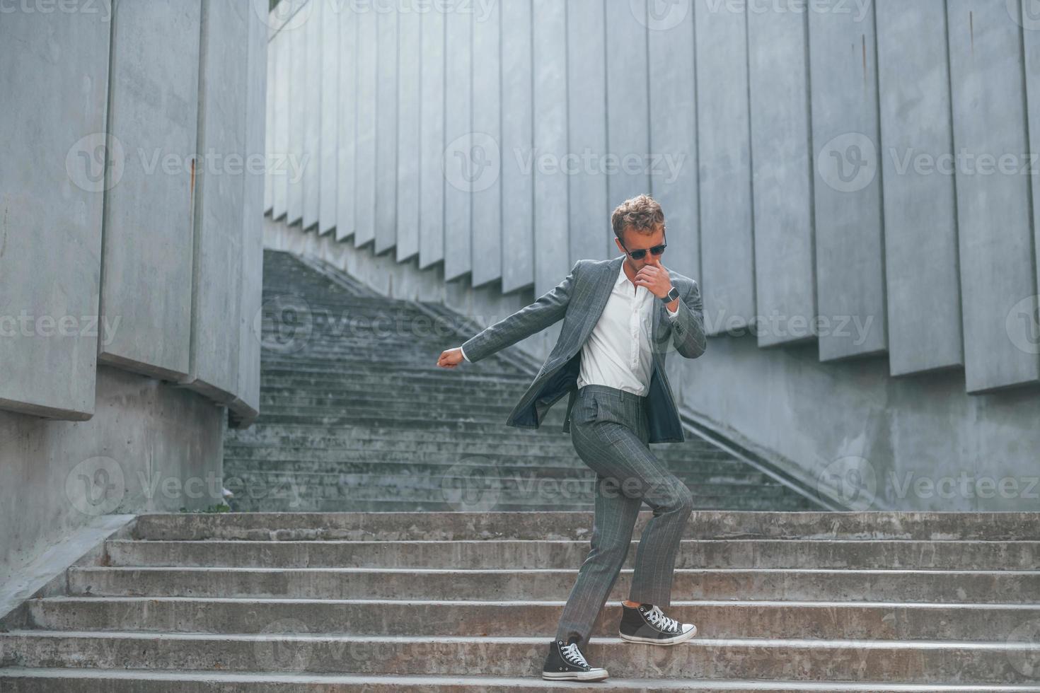 Dancing, celebrating success. Young businessman in grey formal wear is outdoors in the city photo