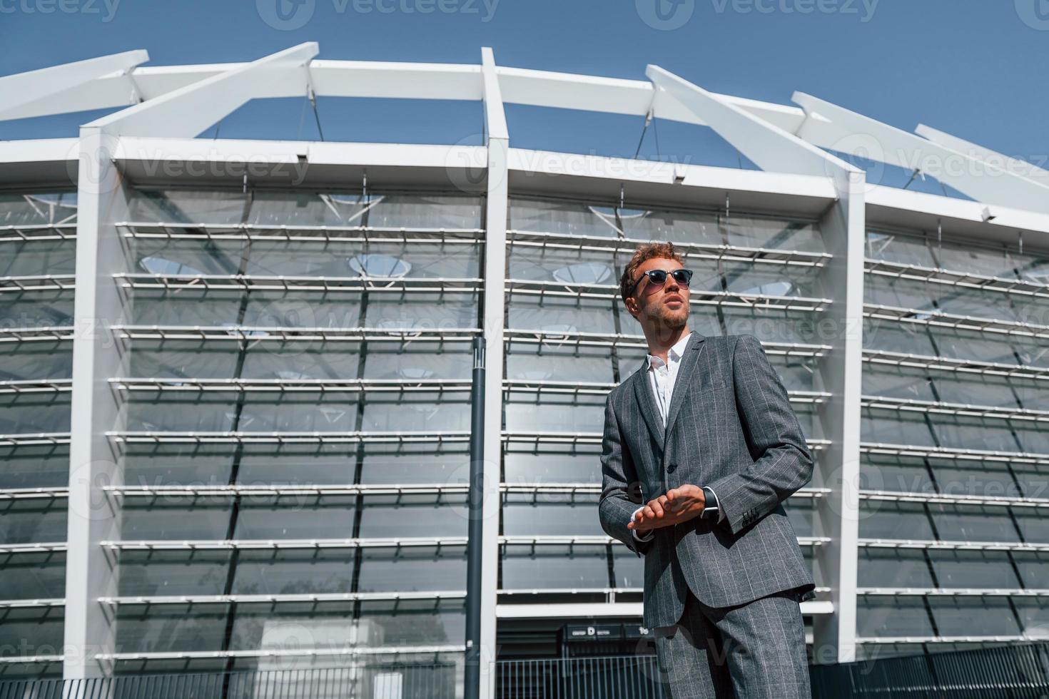 gran estadio detrás. un joven hombre de negocios con ropa formal gris está al aire libre en la ciudad foto