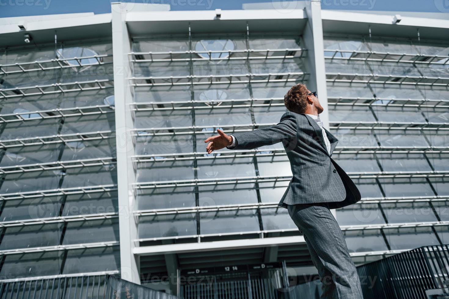 Dancing, celebrating success. Young businessman in grey formal wear is outdoors in the city photo