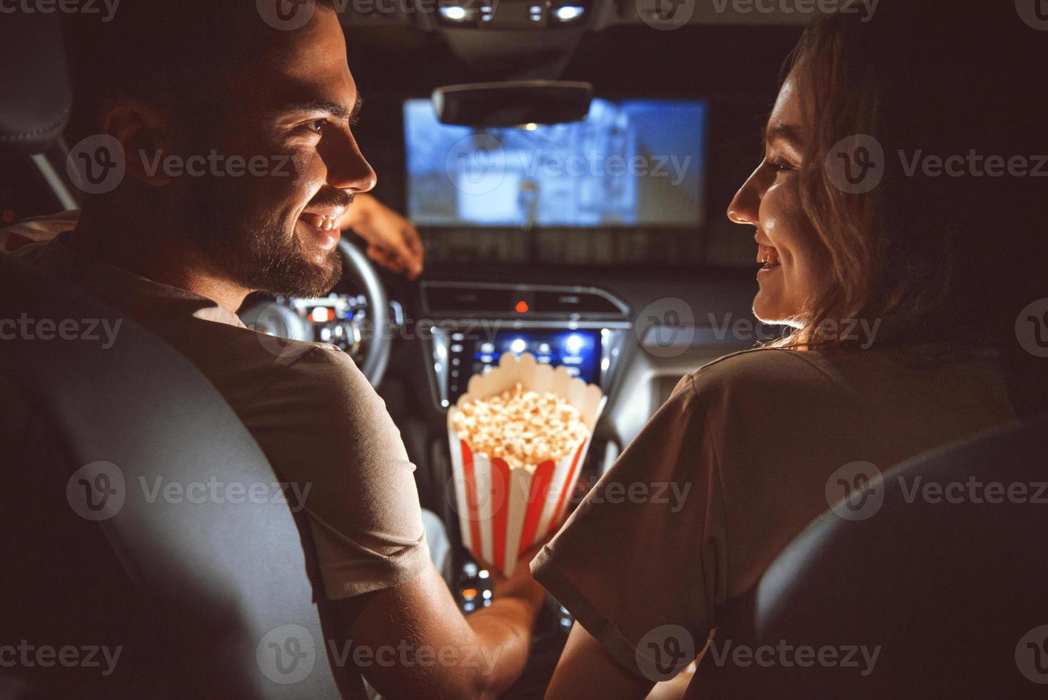 Beautiful happy young couple sitting in the car together and eating popcorn photo