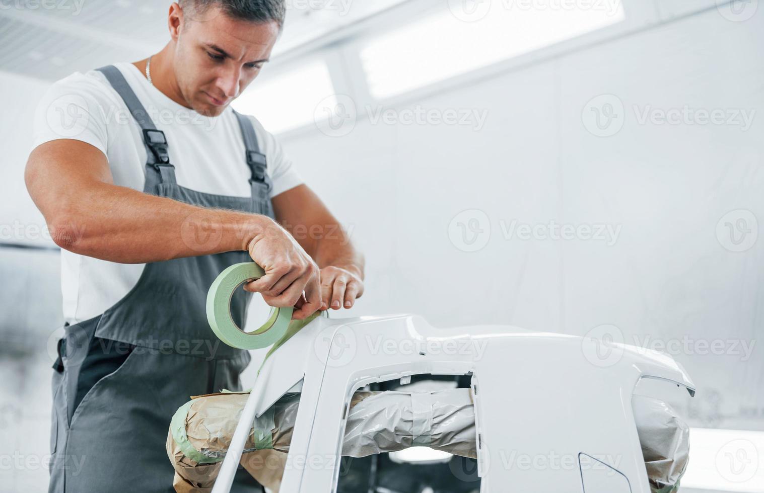 Works with car hood. Caucasian automobile repairman in uniform in garage photo