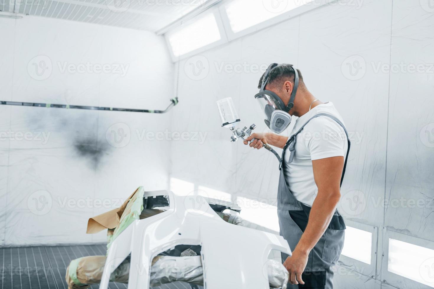 Uses painting gun. Caucasian automobile repairman in uniform works in garage photo