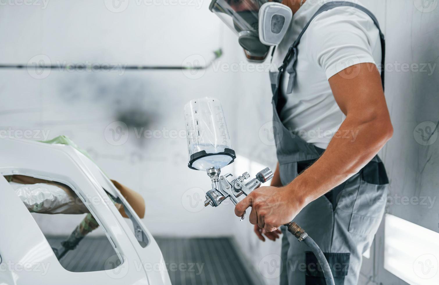 con pistola de pintura. reparador de automóviles caucásico en uniforme trabaja en garaje foto