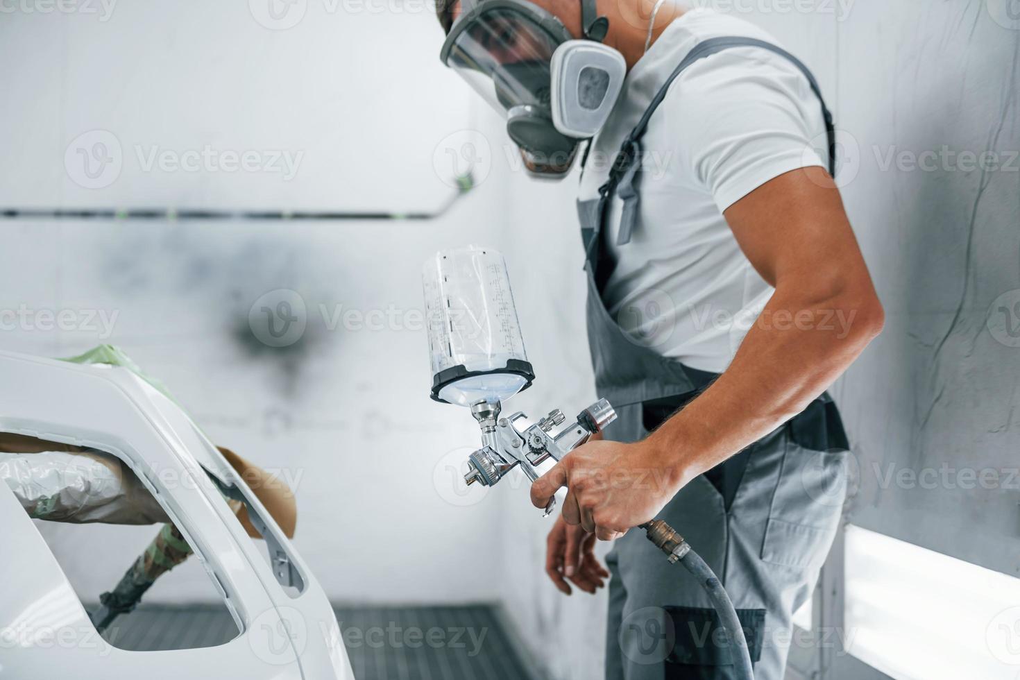 con pistola de pintura. reparador de automóviles caucásico en uniforme trabaja en garaje foto