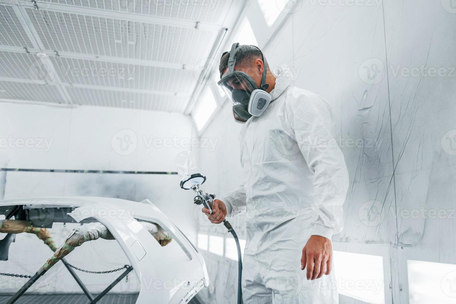 In protective mask. Painting the car. Caucasian automobile repairman in uniform works in garage photo