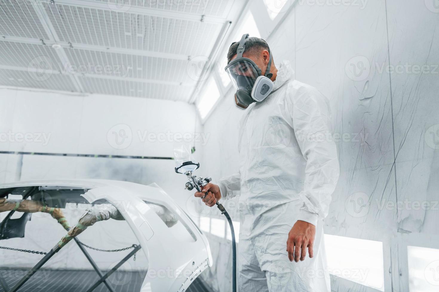 In protective mask. Painting the car. Caucasian automobile repairman in uniform works in garage photo