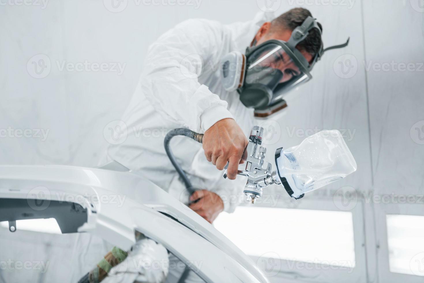 In protective mask. Painting the car. Caucasian automobile repairman in uniform works in garage photo