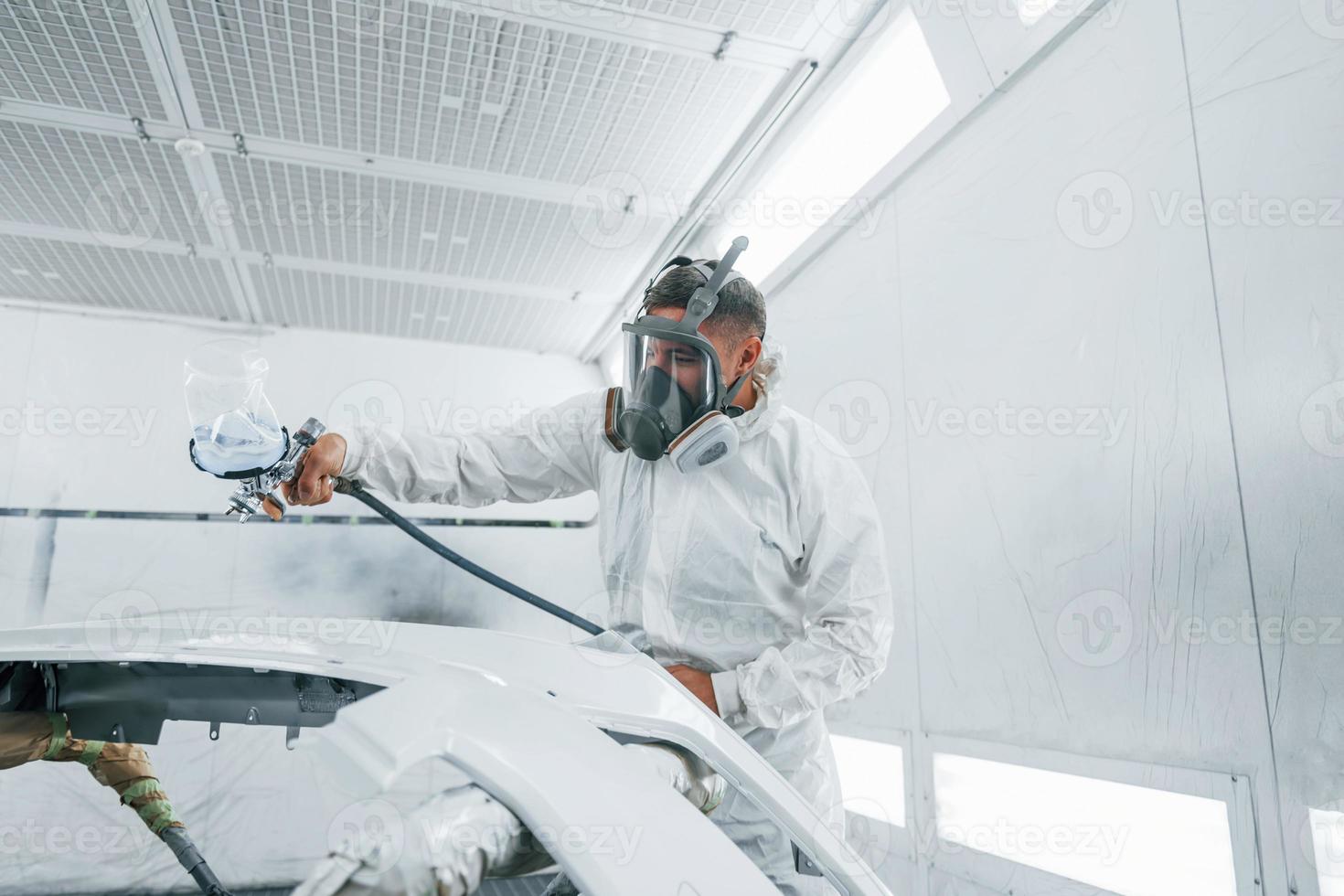 In protective mask. Painting the car. Caucasian automobile repairman in uniform works in garage photo