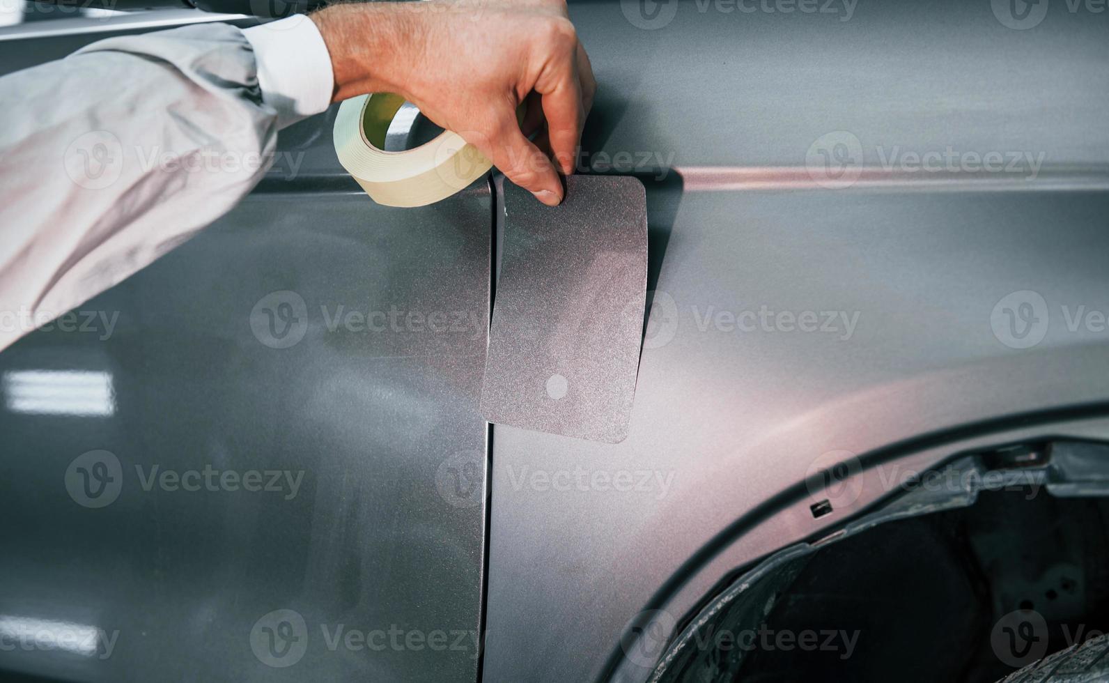 Applying new color. Caucasian automobile repairman in uniform works in garage photo