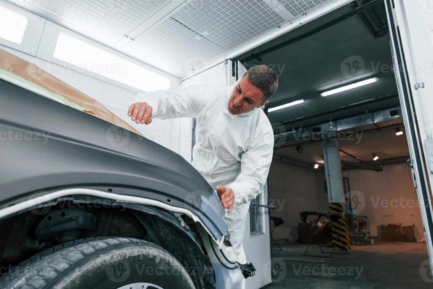 Covering car by brown cloth. Caucasian automobile repairman in uniform works in garage photo