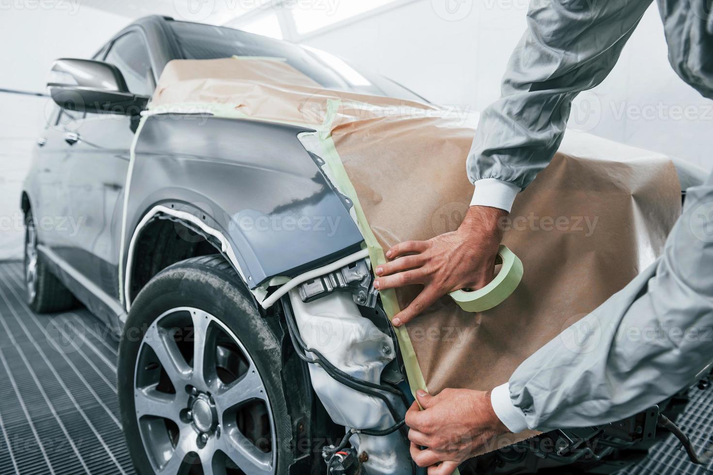 Covering car by brown cloth. Caucasian automobile repairman in uniform works in garage photo