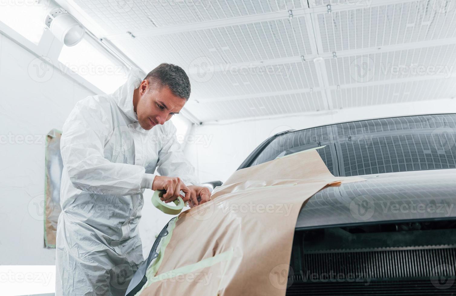 cubriendo el coche con tela marrón. reparador de automóviles caucásico en uniforme trabaja en garaje foto