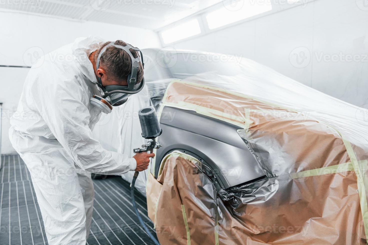 Painting job in progress. Caucasian automobile repairman in uniform works in garage photo