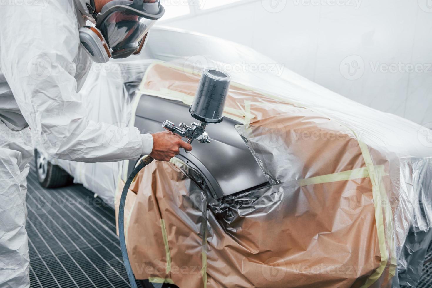 Painting job in progress. Caucasian automobile repairman in uniform works in garage photo