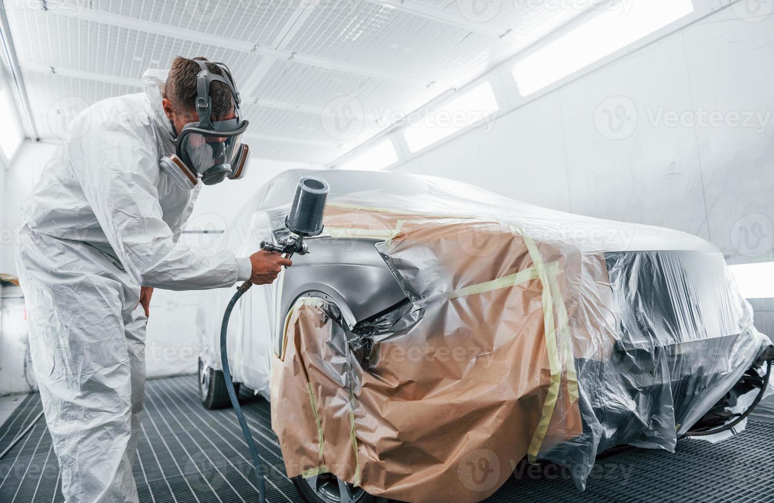 trabajo de pintura en curso. reparador de automóviles caucásico en uniforme trabaja en garaje foto