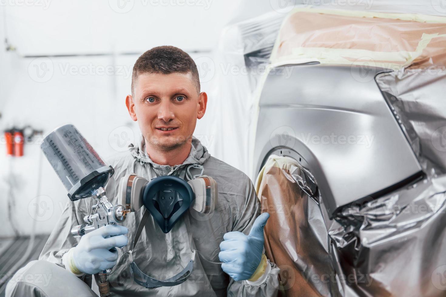 Sits near freshly painted car. Caucasian automobile repairman in uniform works in garage photo