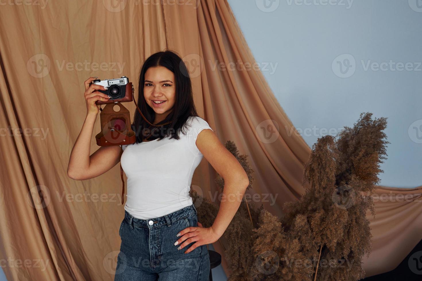 una joven alegre se mantiene adentro y tiene una cámara retro foto