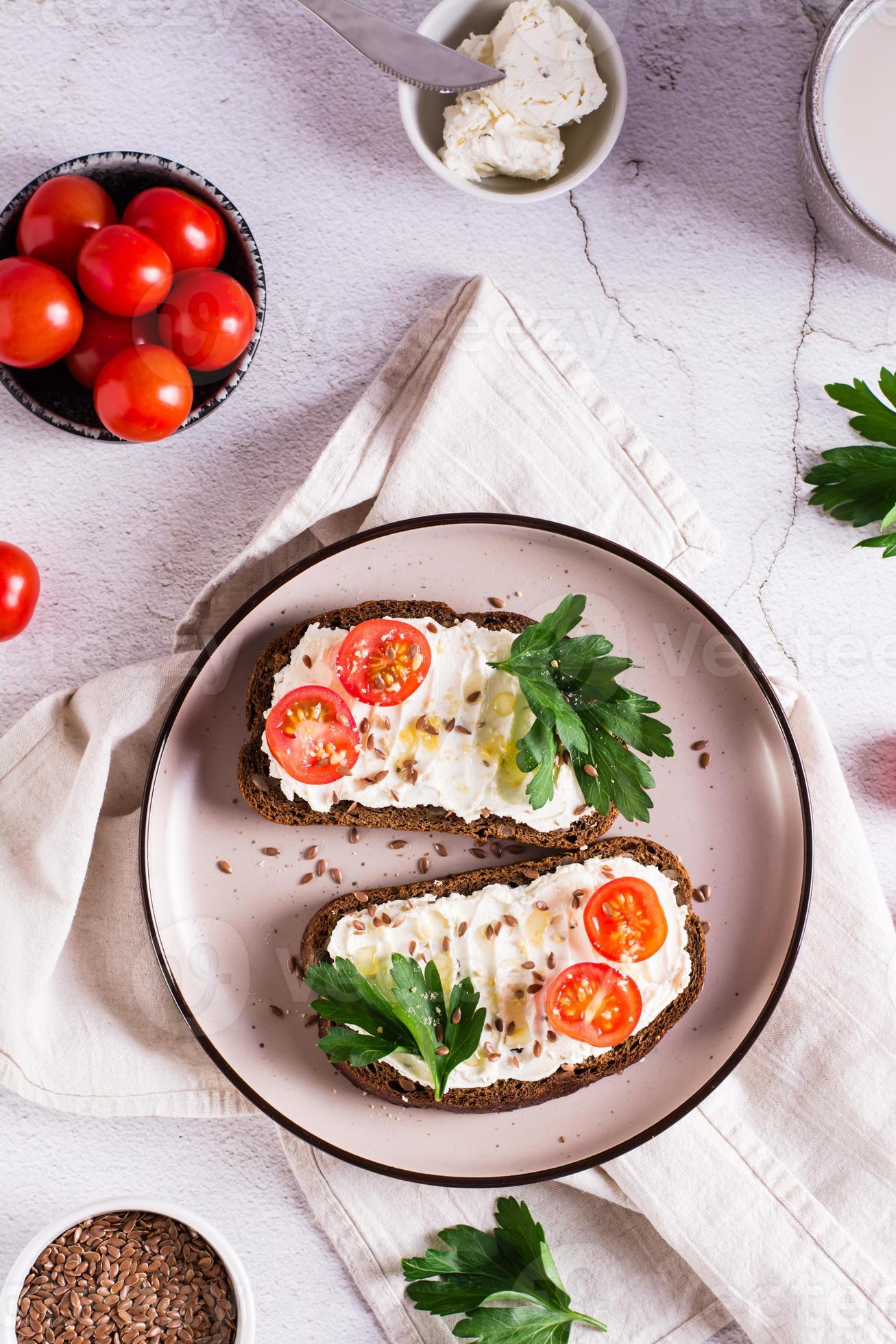 Sandwiches on rye bread with ricotta, tomatoes and parsley on a plate