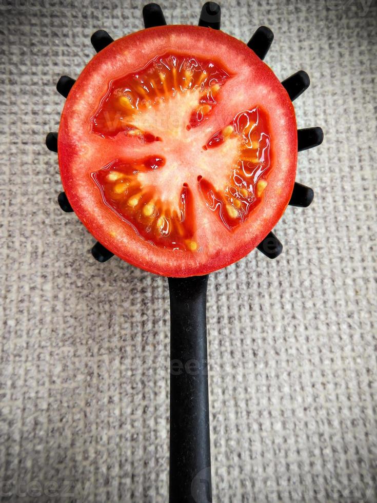 Half tomato on a toothed kitchen spoon on a gray ground. Vertical image. photo