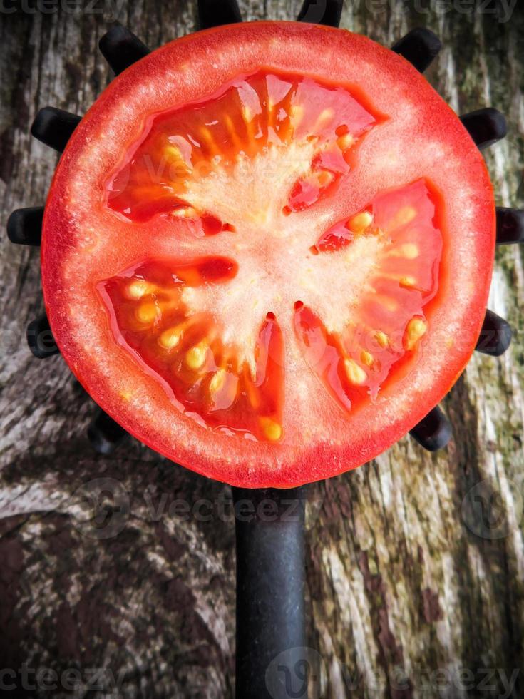 Half tomato on a toothed kitchen spoon on a old wooden table. Vertical image. photo