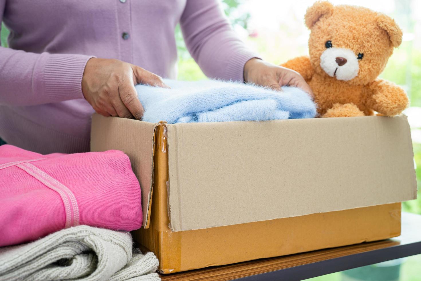Holding clothing donation box with used clothes and doll at home to support help for poor people in the world. photo