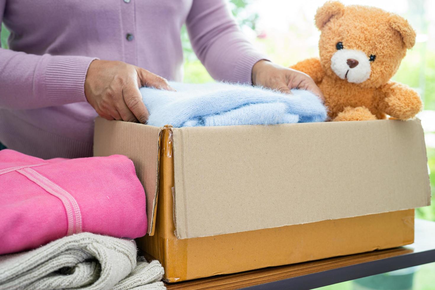 sosteniendo una caja de donación de ropa con ropa usada y muñecas en casa para apoyar la ayuda a los pobres del mundo. foto