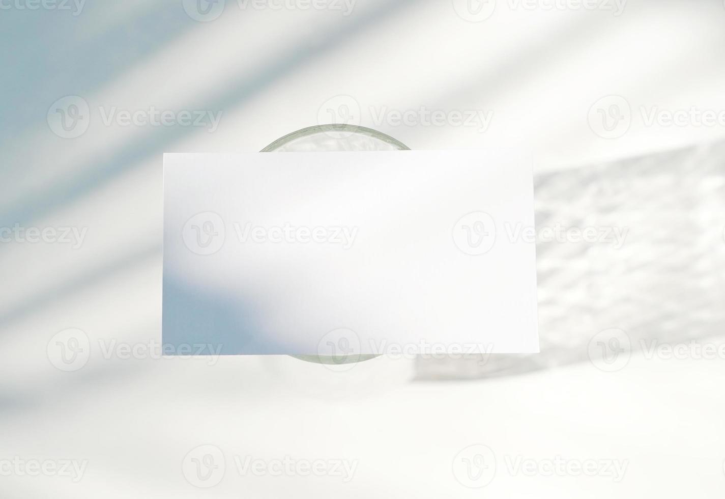 Blank business card mockup on glass with shade of natural leaves shadow overlay on white background, for product or presentation photo