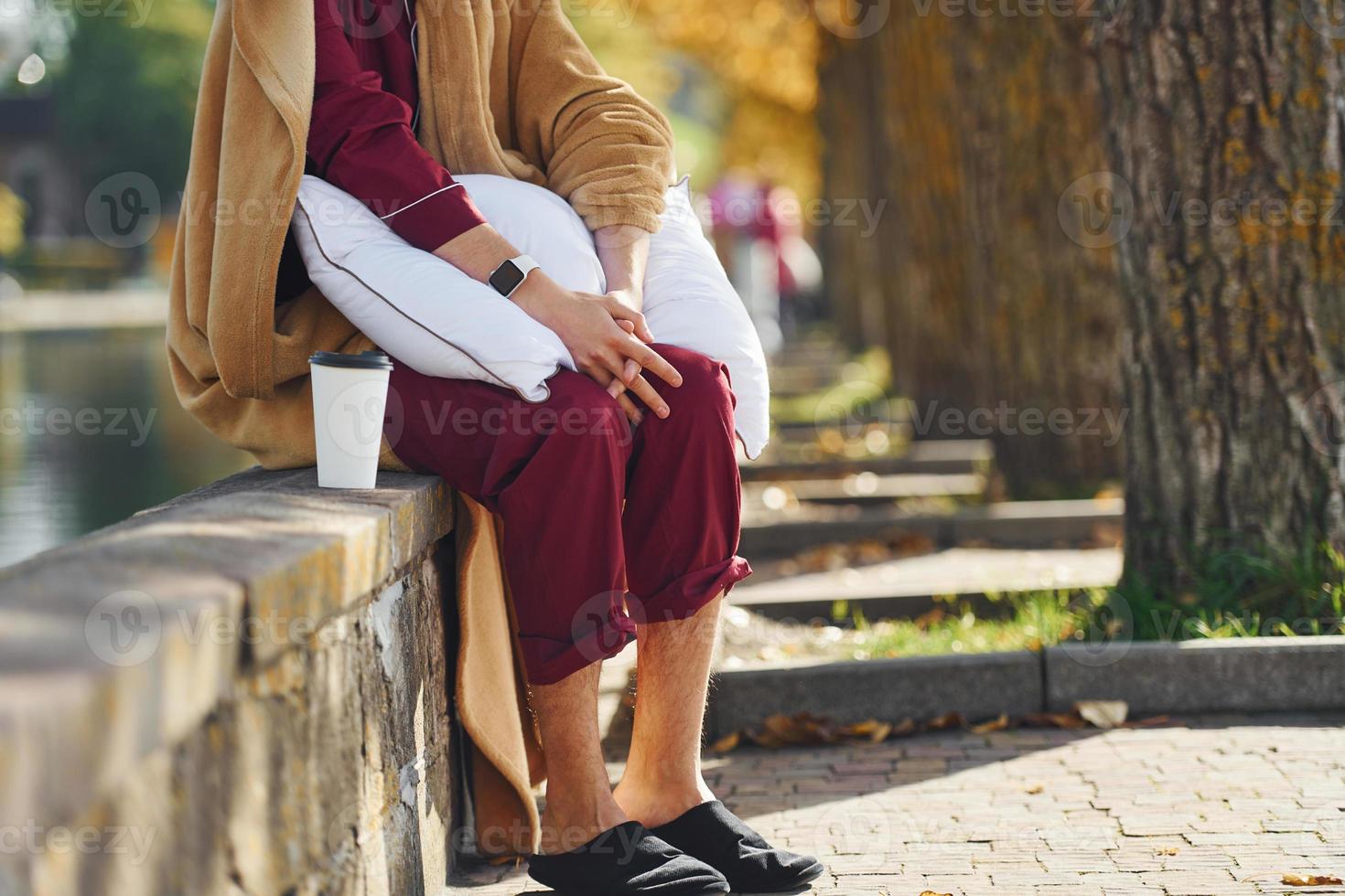 en el parque con taza de bebida. joven en pijama está al aire libre en la calle. se siente somnoliento foto