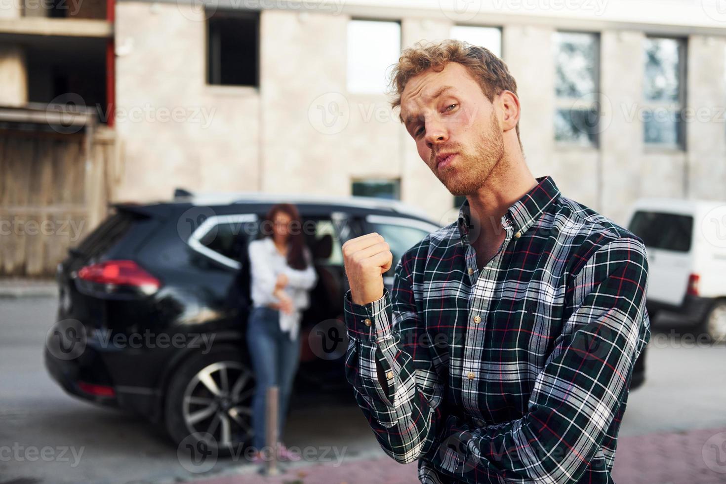 Man in fashionable clothes standing in front of girl that is near the black automobile photo