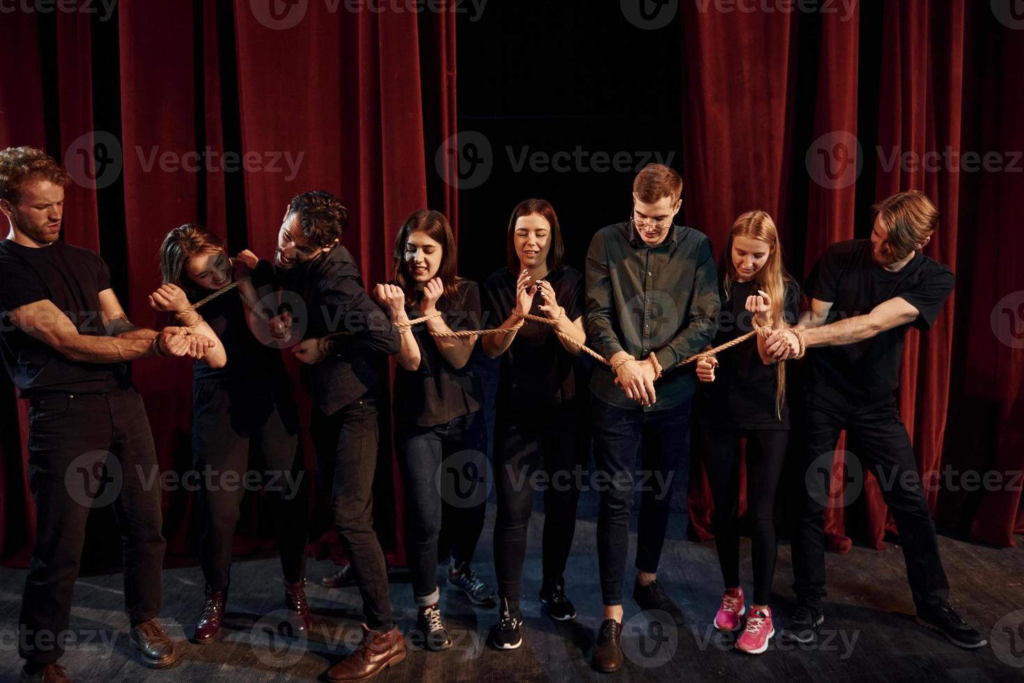 con cuerda en las manos. grupo de actores con ropa de color oscuro ensayando en el teatro foto