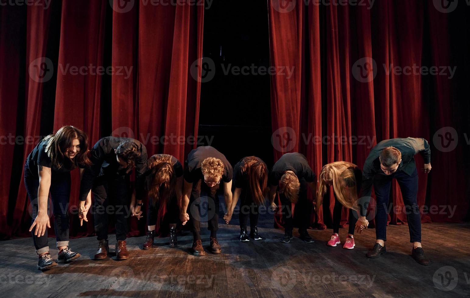People bowing to audience. Group of actors in dark colored clothes on rehearsal in the theater photo