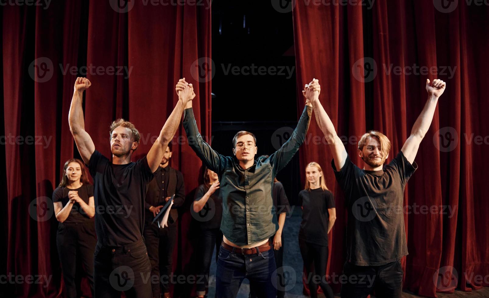 With hands up. Conception of success. Group of actors in dark colored clothes on rehearsal in the theater photo