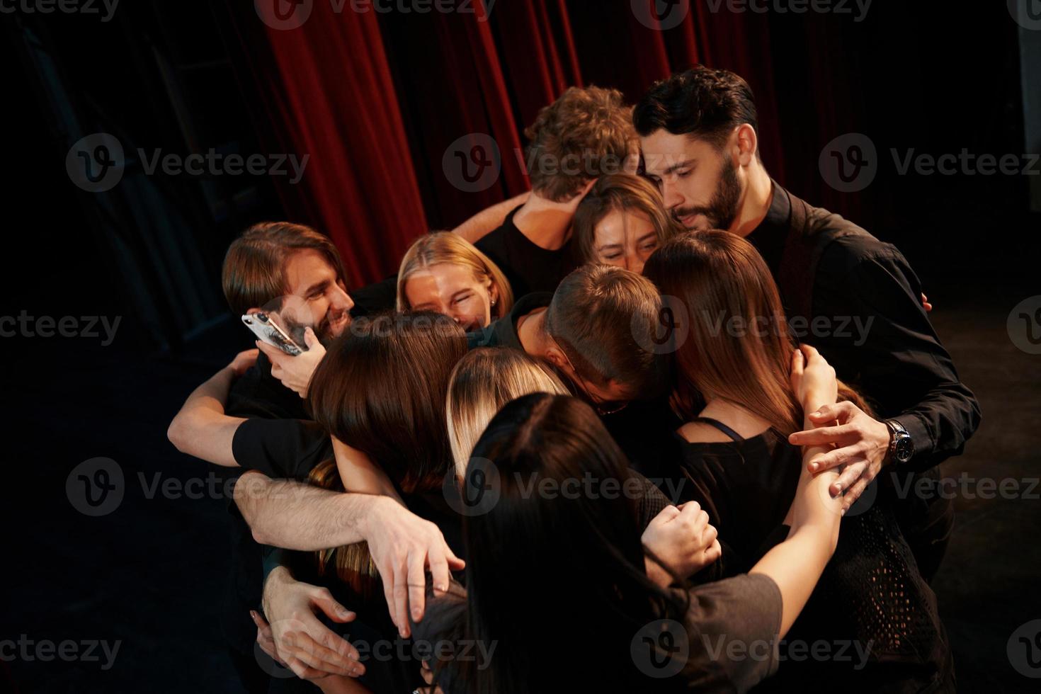 abrazándose unos a otros. grupo de actores con ropa de color oscuro ensayando en el teatro foto