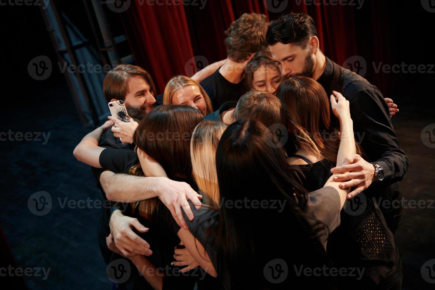 Embracing each other. Group of actors in dark colored clothes on rehearsal in the theater photo