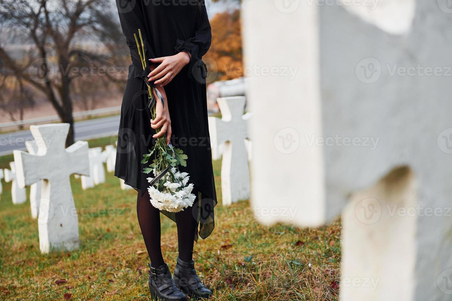 con flores en las manos. joven vestida de negro visitando el cementerio con muchas cruces blancas. concepción del funeral y la muerte foto