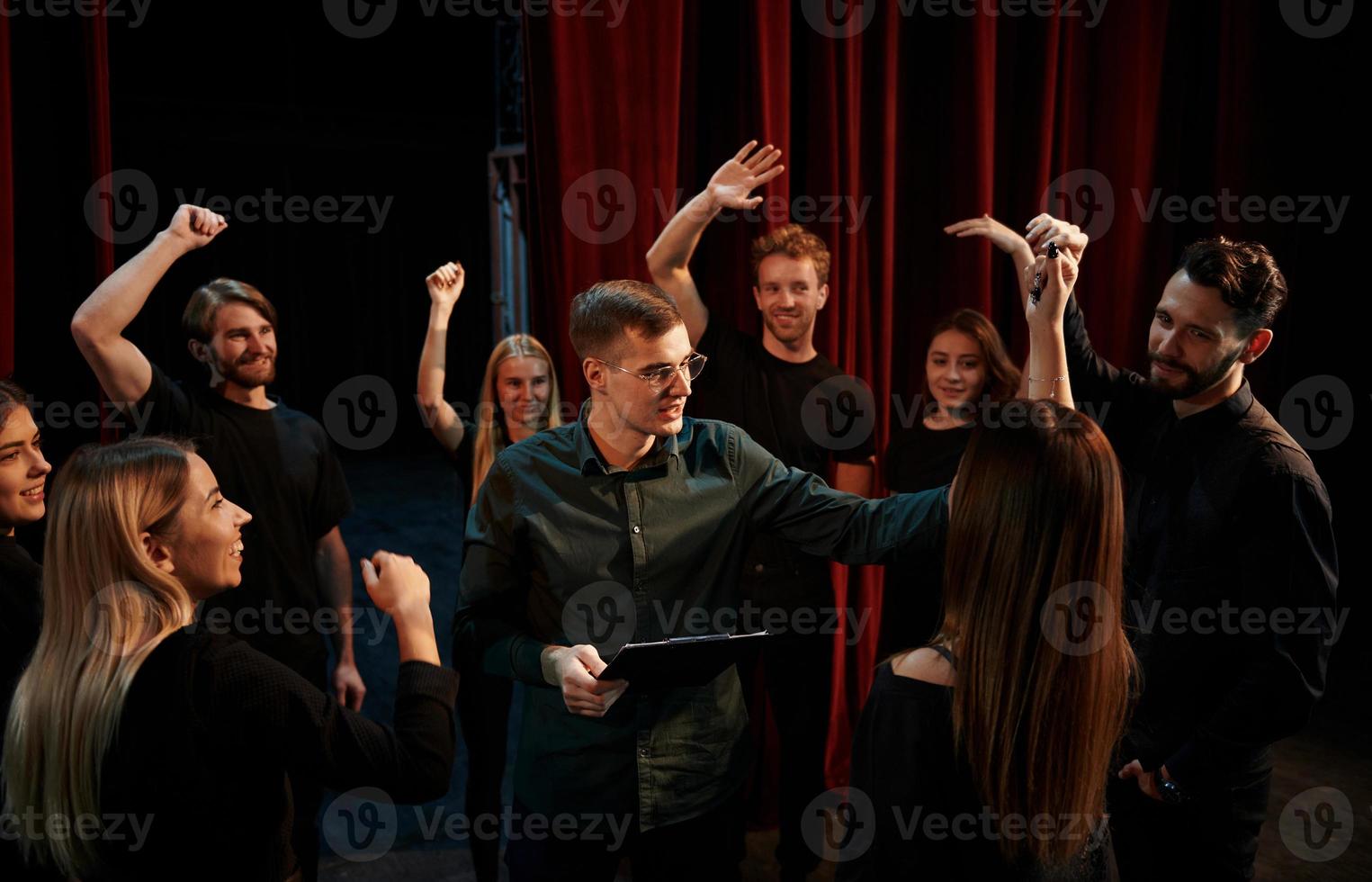 Happy people celebrating success. Group of actors in dark colored clothes on rehearsal in the theater photo